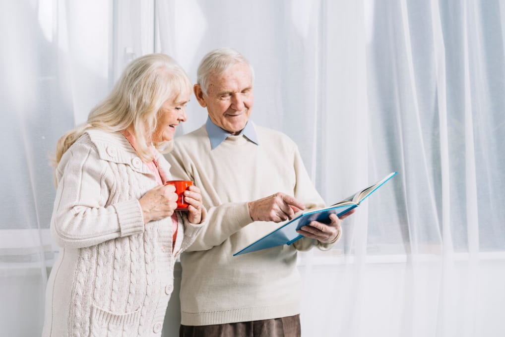 An elderly couple sharing a moment over a book with a cup of tea