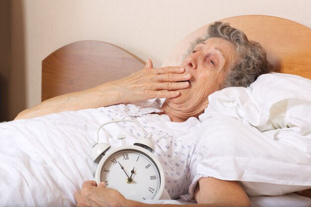 An old woman yawns while holding an antique alarm clock