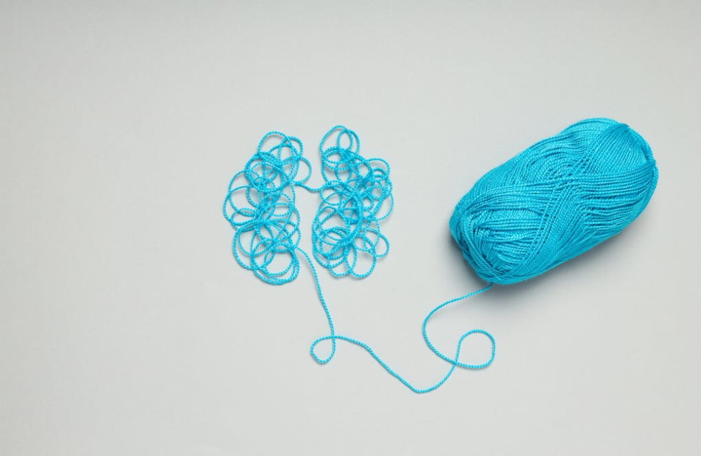 A tangle of blue yarn beside a neat skein on a white background